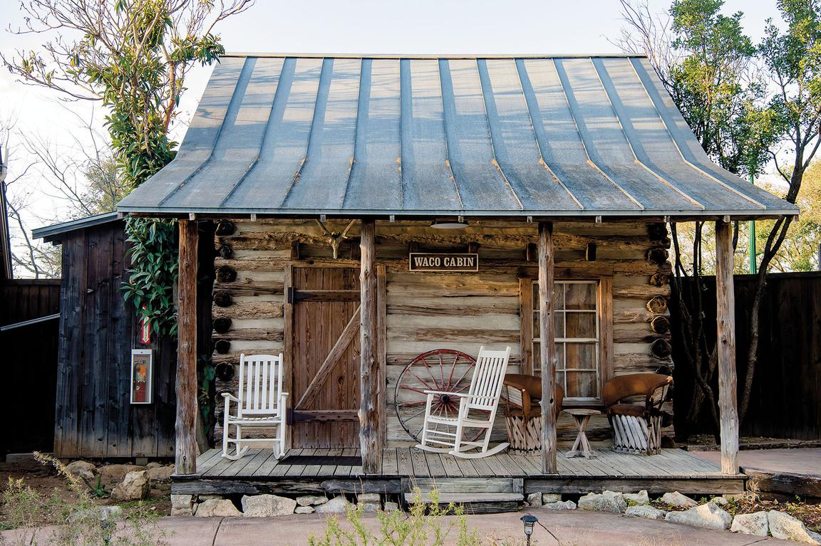 The exterior of a meager log cabin with a tin roof and a small sign reading 'Waco Cabin'
